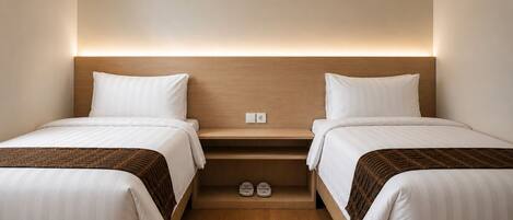 A hotel room with two beds, a wooden headboard, a shelf with shoes, and a wall socket.