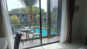A hotel room with a large window, a bed, a chair, and a view of a swimming pool and greenery. - Sea Panwa Beach (Wichit)