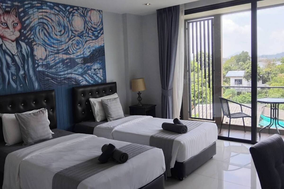 Une chambre d’hôtel avec deux lits, une grande fenêtre donnant sur un beau paysage, un tableau au mur et un balcon avec une table et des chaises.