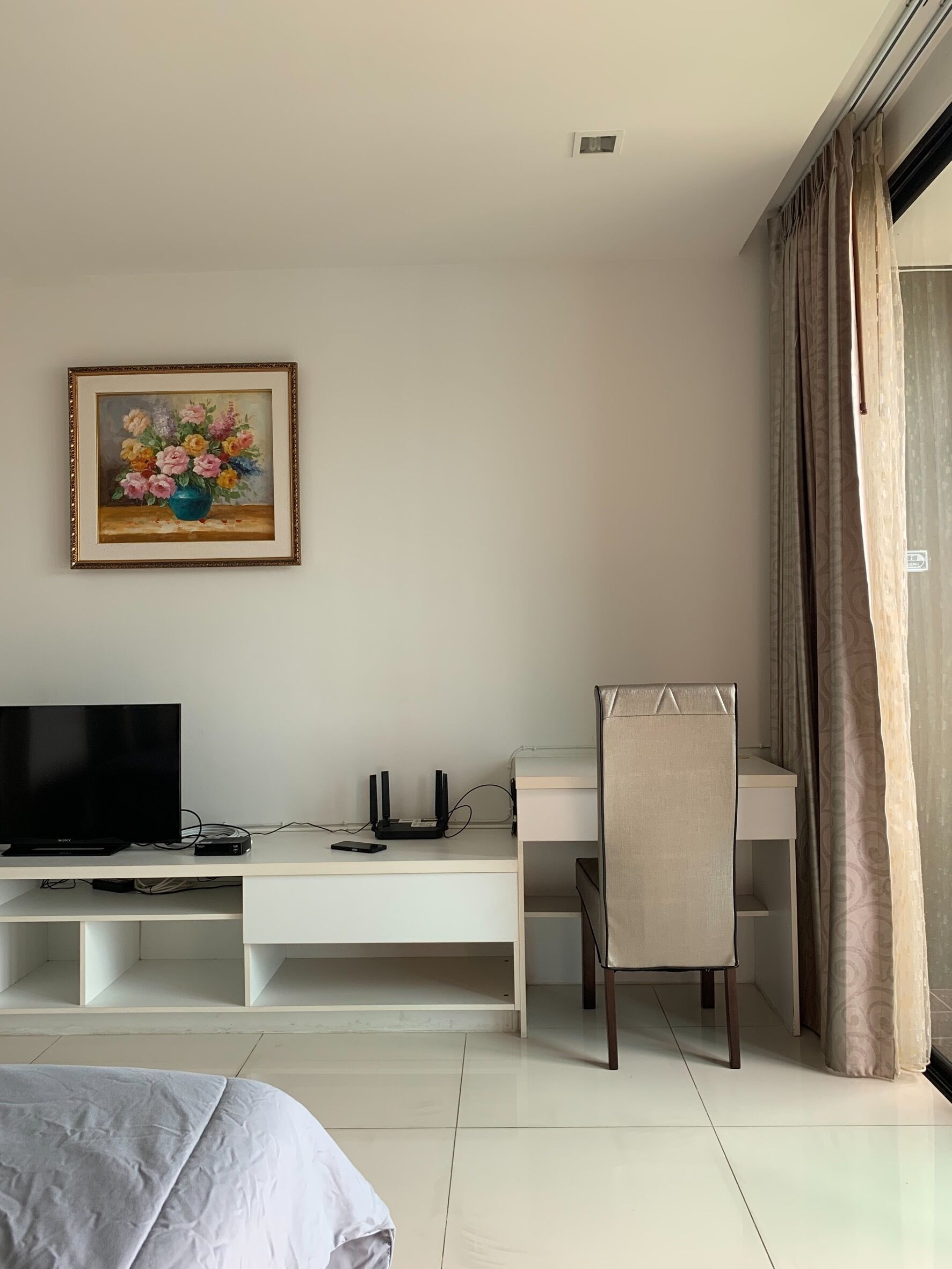 A hotel room with a bed, a desk with a chair, a television, and a framed painting on the wall.