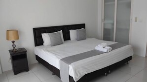 A neatly made bed with white linens, a bedside lamp, and a small nightstand. - Sea Panwa Beach (Wichit)