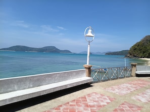 A coastal walkway with a metal railing, a white lamp post, and a bench. - Sea Panwa Beach (Wichit)