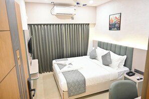 Hotellihuone, jossa on sänky, työpöytä puhelimineen, seinälle asennettu ilmastointilaite ja taulu.