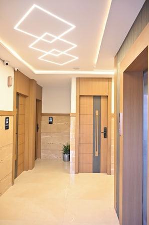 A modern hallway with wooden doors, a marble floor, and a geometric ceiling light design.