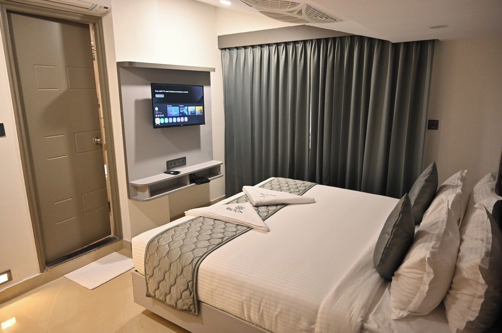Ein Hotelzimmer mit Bett, einem an der Wand befestigten Fernseher, einem Schreibtisch mit Stuhl und einer Tür.