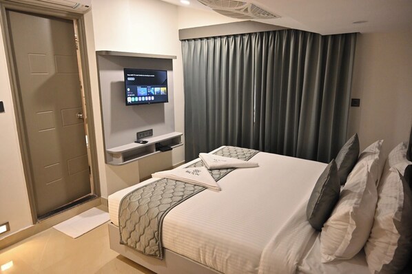A hotel room with a bed, a TV mounted on the wall, a desk with a chair, and a door. - Bilton Premium Luxury Hotel Koramangala (Bengaluru,)