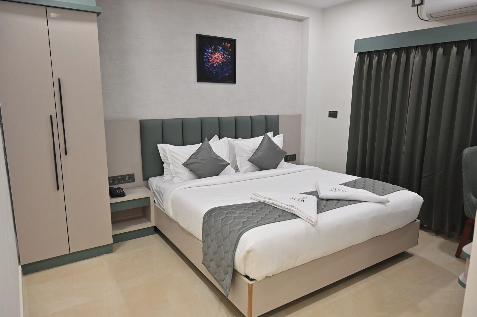 Una habitación de hotel moderna con una cama grande, cabecero gris y una mesita de noche.
