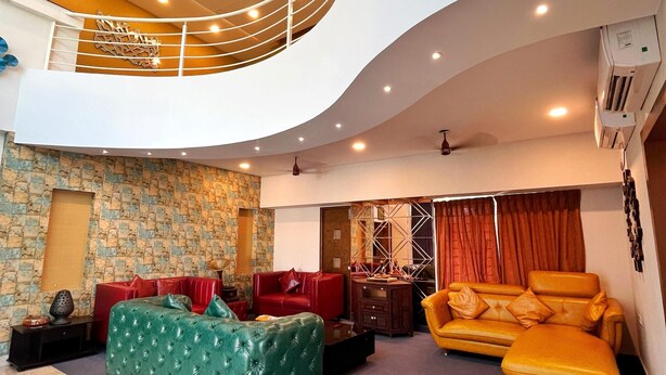 A spacious living area with a high ceiling, a balcony, and a modern chandelier. - The Charlie Suites (Chennai)