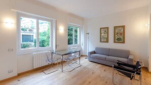 Una sala de estar moderna con una mesa de comedor de vidrio, un sofá gris y una silla negra.