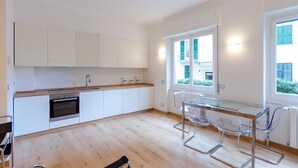 Una cocina moderna con armarios blancos, un horno de acero inoxidable y una mesa de comedor de vidrio con sillas.