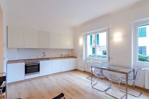 A modern kitchen with white cabinets, a stainless steel oven, and a glass dining table with chairs. - 2 Flats Combined Spacious Family Retreat (Santa Margherita Ligure)