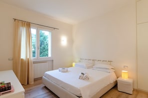 A clean, minimalist bedroom with a large bed, bedside lamps, and a view of greenery outside. - 2 Flats Combined Spacious Family Retreat (Santa Margherita Ligure)