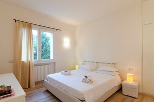 Camera da letto pulita e dal design minimalista, con un letto grande, lampade ai comodini e vista sul verde.