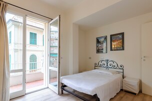 Una camera da letto con un letto, un comodino, una porta e un balcone con vista sugli edifici.