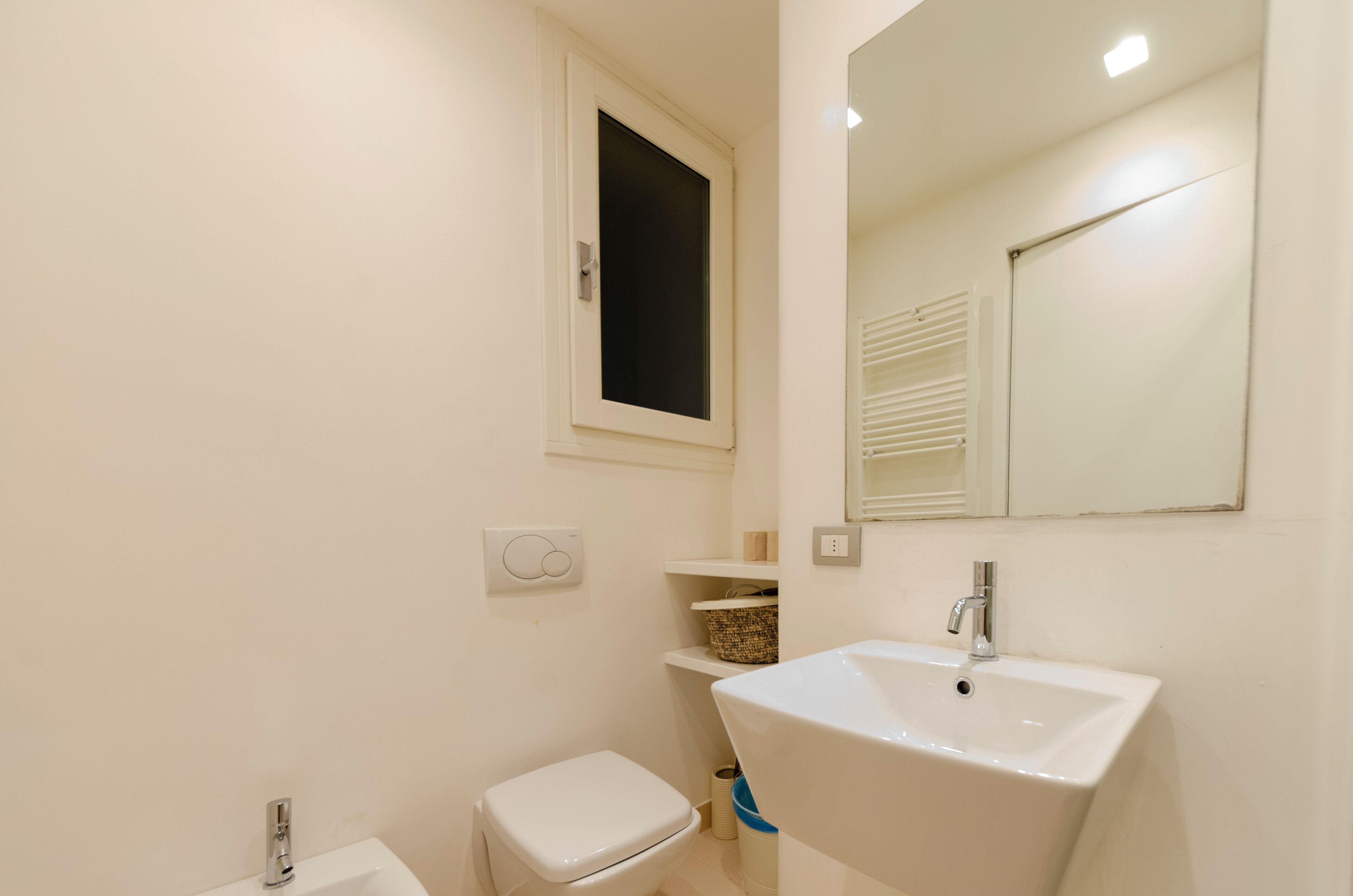Ein kleines, sauberes Badezimmer mit einem weißen Waschbecken, einer Toilette und einem Fenster über der Toilette.