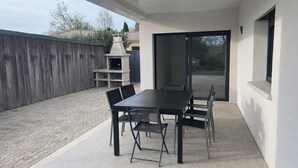 Eine Terrasse im Freien mit Tisch und Stühlen, einem Steinofen und einer Schiebetür zu einem überdachten Bereich.