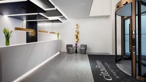 A modern hotel reception area with a reception desk, two chairs, a small table with a vase, and a wall-mounted decorative piece. - Shanghai Citadines Hotel (Lujiazui Financial District Beiyangjing Road Subway Station Branch) (Shanghai)