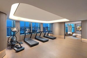 A modern gym with treadmills, exercise bikes, and a large window overlooking a cityscape.