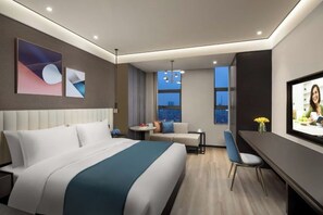 A modern hotel room with a large bed, a desk, a TV, and a view of the city at night.