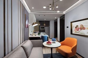 A modern hotel room with a sofa, an orange chair, a small table, a kitchen area, and a framed picture on the wall. - Shanghai Citadines Hotel (Lujiazui Financial District Beiyangjing Road Subway Station Branch) (Shanghai)