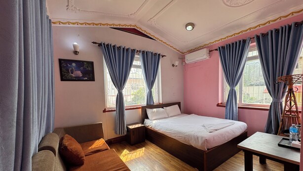 A bedroom with a bed, a sofa, a table, and a window with curtains. - 555 Home Stay and Restaurant (Burhanilkantha)