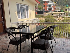 Un balcon avec une table en verre et des chaises en osier, une porte et une fenĂȘtre avec des barreaux en mĂ©tal.