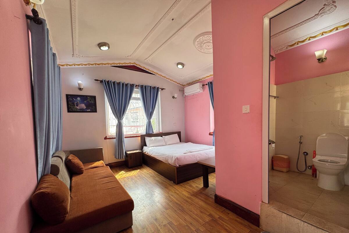 A bedroom with a bed, a sofa, a window with curtains, a shower area, and a toilet.