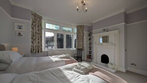 Une chambre avec deux lits, une cheminée, une bibliothèque et une fenêtre avec des rideaux.