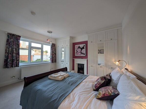 Un dormitorio con cama, ventana con cortinas, chimenea y armario.