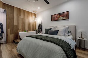 Ein modernes Schlafzimmer mit einem großen Bett, einer eingebauten Badewanne und einem an der Wand befestigten abstrakten Gemälde.