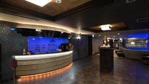 A hotel reception area with a curved counter, a blue-lit backdrop, and a tiled floor. - Hotel Bvljua -leisure hotel- Adults Only (Kurume)