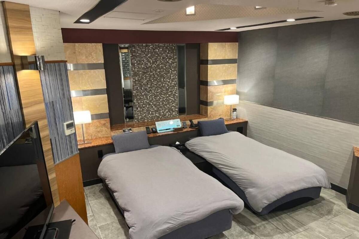 A hotel room with two beds, a desk with a computer, a TV, and a mirror.