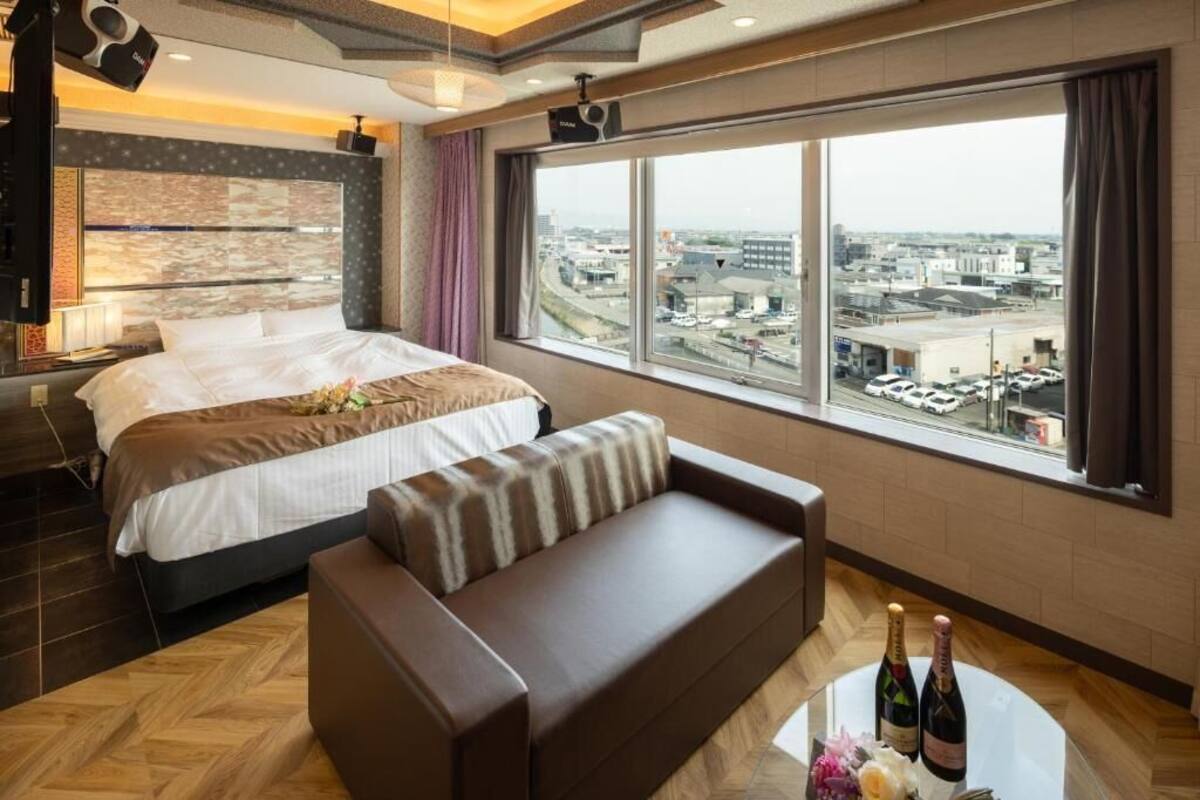 A hotel room with a large bed, a sofa, a view of the city, and a table with bottles.