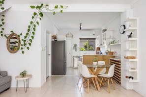 A modern kitchen with a central island, white cabinetry, and a dining area with a glass table and chairs. - Opal Sands: Steps from the Beach. (HERVEY BAY)