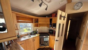 A compact kitchen with wooden cabinets, a sink, a stove, and a microwave.