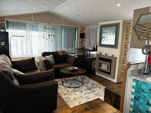 A living room with a sofa, armchair, coffee table, and fireplace. - Lovely and Comfy 3-Bedroom Mobile Home Retreat in Kirkcolm (Kirkcolm)