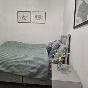 A bedroom with a bed, pillows, a bedside table with a vase, and two framed botanical prints on the wall. - Cozy Room • Quick Central London Access (Greater London)