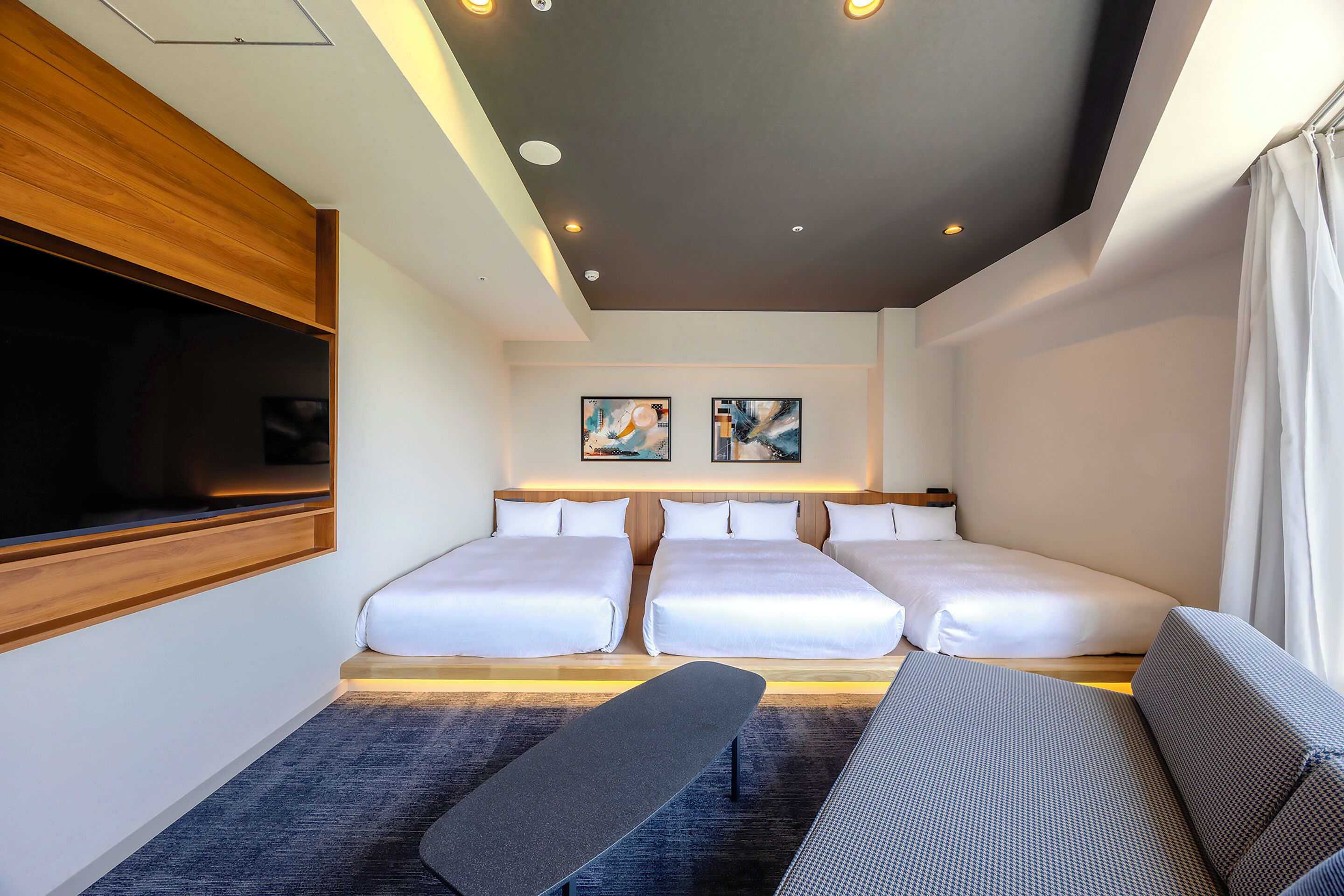 A hotel room with two beds, a bench, a TV, and artwork on the wall.