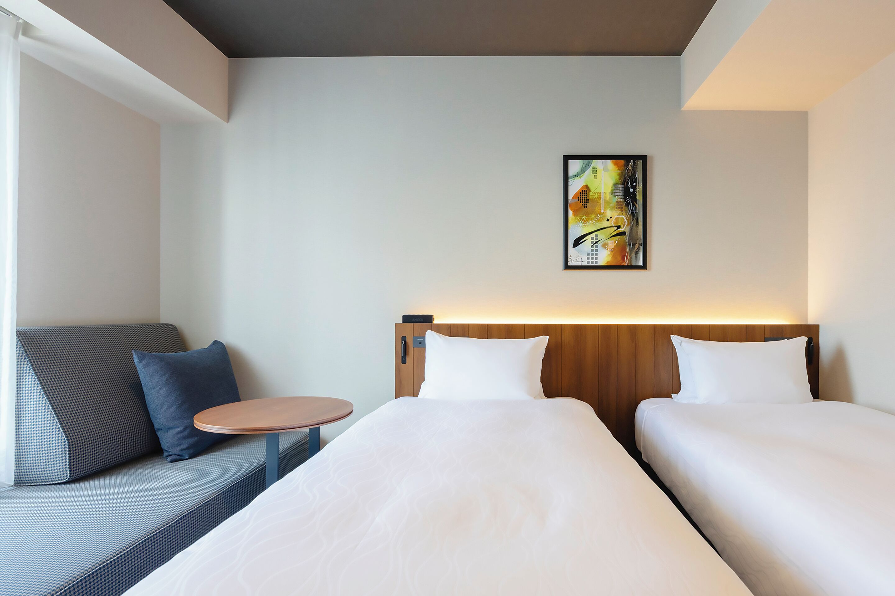 A hotel room with two beds, a sofa, a small round table, and a painting on the wall.