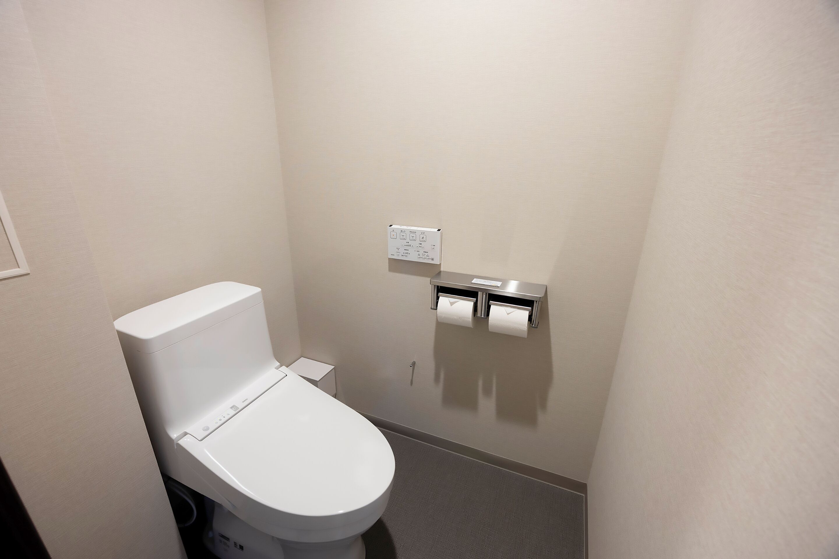 Et standard badeværelse med toilet, papirhåndklædeholder og skyl.'