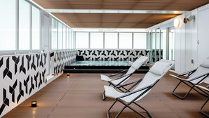 A modern indoor pool area with lounge chairs, a patterned wall, and a ceiling with wooden slats.