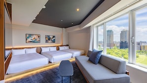 A hotel room with a large window, two beds, a sofa, and artwork on the wall.