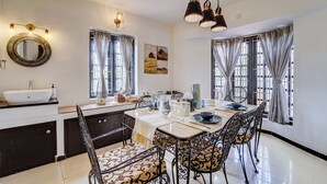 A dining area with a table set for four, a round mirror, and a window with curtains. - Alaya Stays Cleft 3BHK with Garden (Kotagiri)