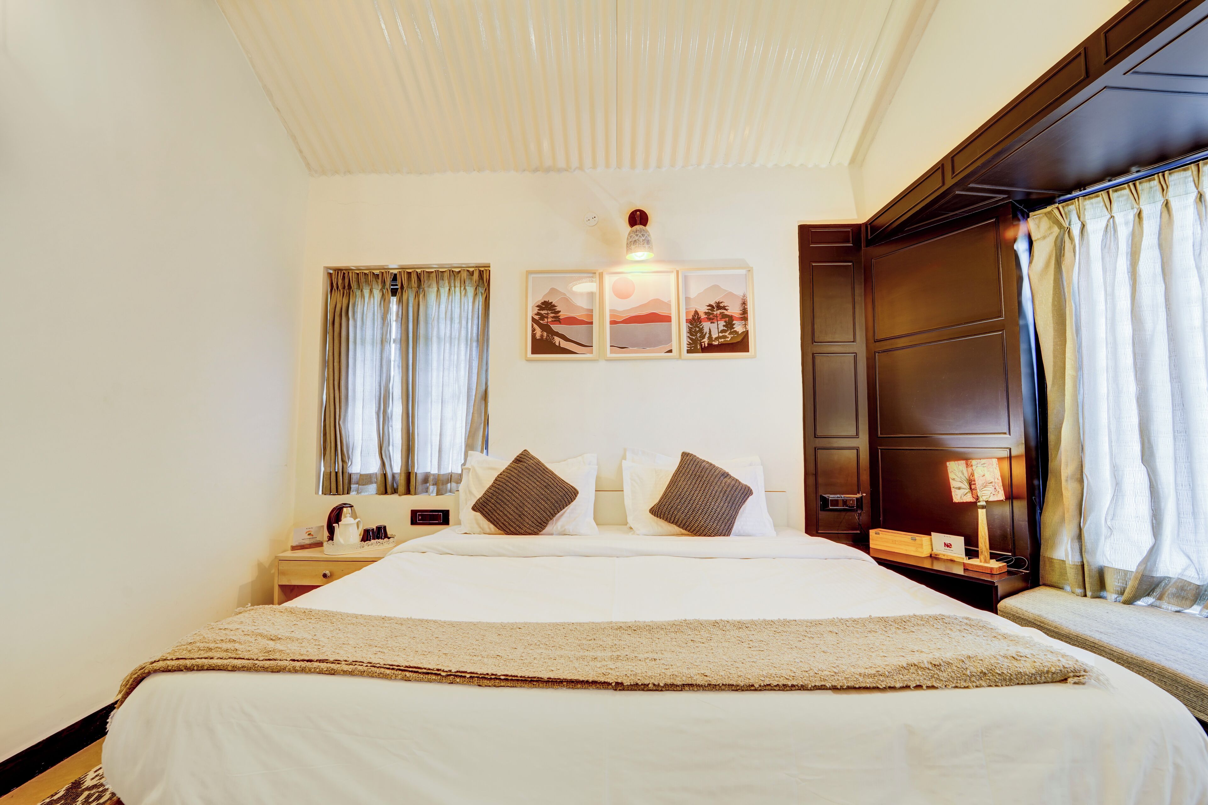 Habitación de hotel con una cama grande, dos mesitas de noche, una lámpara de pared y una ventana con cortinas.