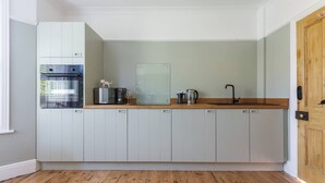 Eine Küche mit weißen Schränken, einer Holztischplatte, einem Edelstahlkühlschrank, einer Kaffeemaschine und einem Wasserkocher.