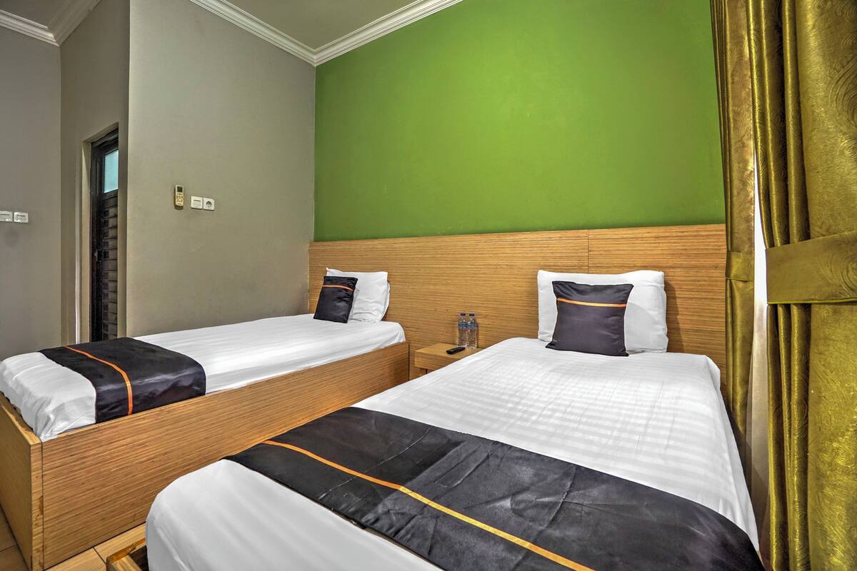 Two single beds with wooden headboards, a green wall, and a gold curtain.