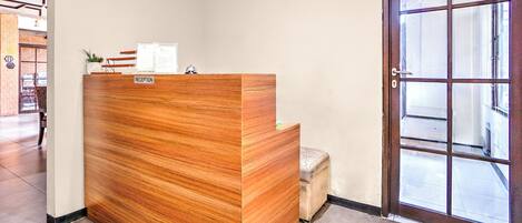 A reception desk with a wooden finish, a reception area, and a glass door leading outside.