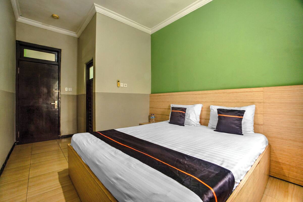 A hotel room with a large bed, a wooden headboard, a green wall, and a wooden floor.