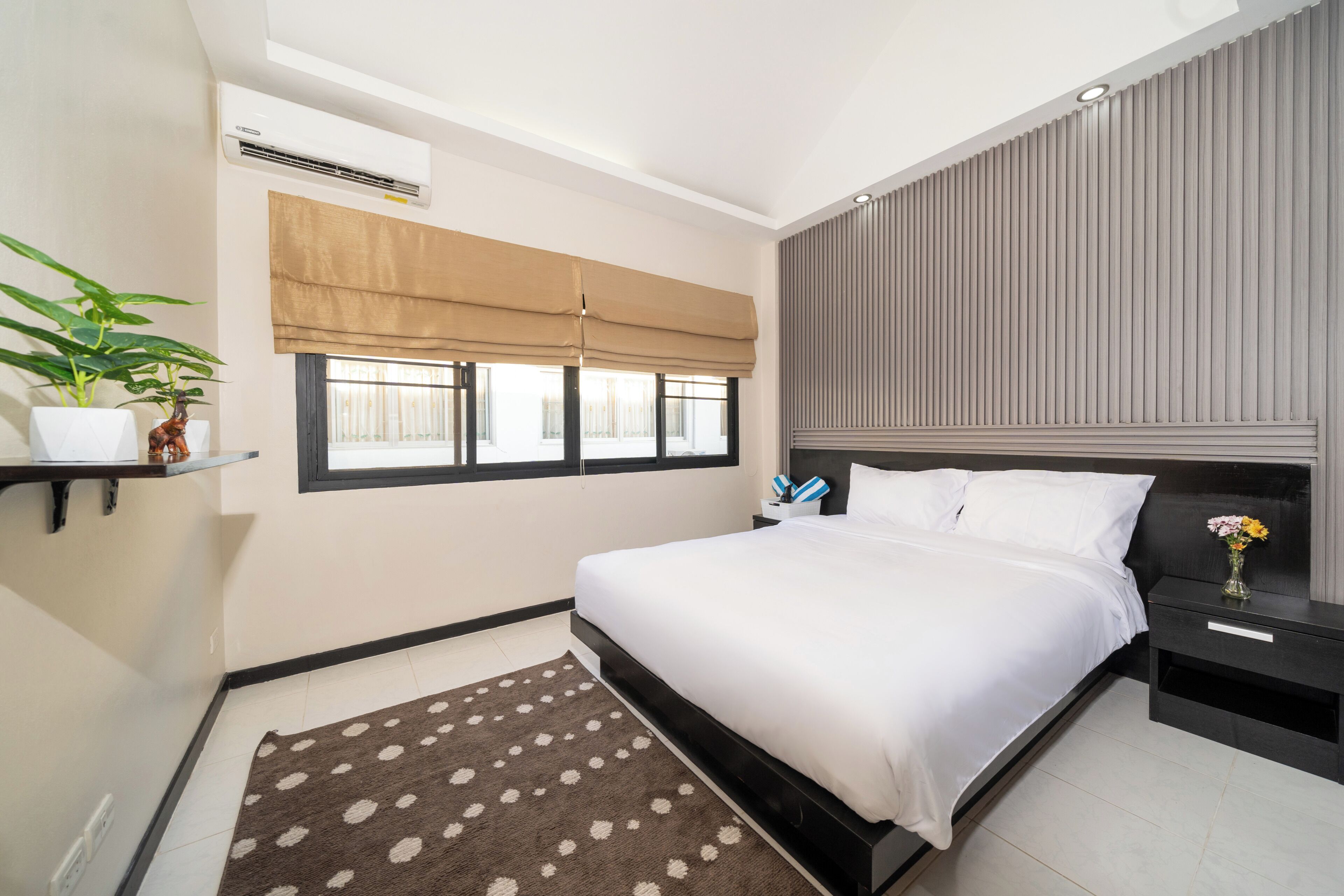 Un dormitorio moderno con cama, mesitas de noche, ventana con persianas, planta en maceta y aire acondicionado instalado en la pared.