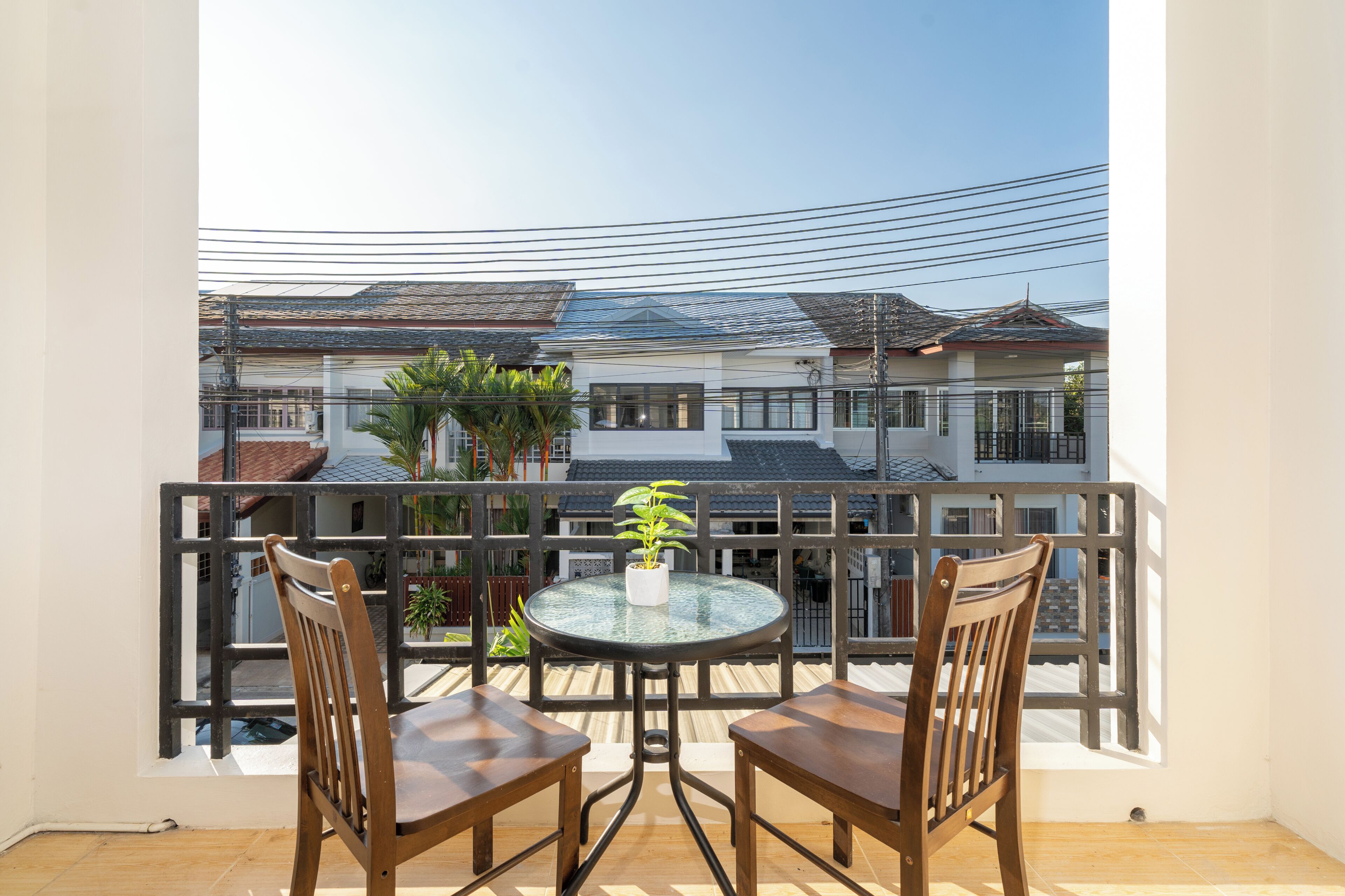 Een balkon met twee houten stoelen, een klein rond tafeltje, een plant in pot en uitzicht op omliggende gebouwen.